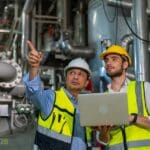 Two professional electrical engineer in safety uniform working together at factory site control room. Industrial engineer worker checking maintenance electric system on laptop computer at plant room.